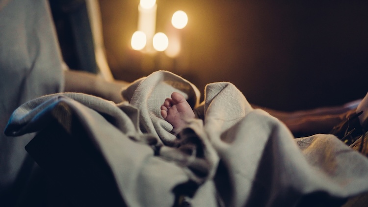 Tiny foot of baby Jesus peeking from soft blankets in a manger, symbolizing the historicity of Jesus and his birth.