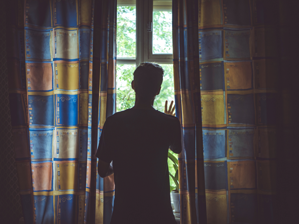 A silhouette of a young man standing in a dark room with his hand on a window, looking out toward the light, visually symbolizing an internal spiritual battle.